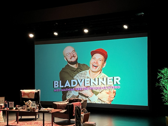Stort lærred med billede af Mathias Helt og Nicholas Nybro, podcastværter på Bladvenner. I forgrunden to lænestole og et sofabord med alverdens nips