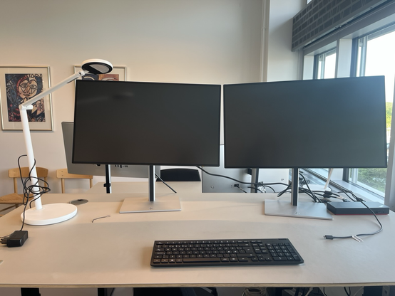 Skrivebord med to store computerskærme, en dockingstation og et tastatur. Ingen mus, dog.