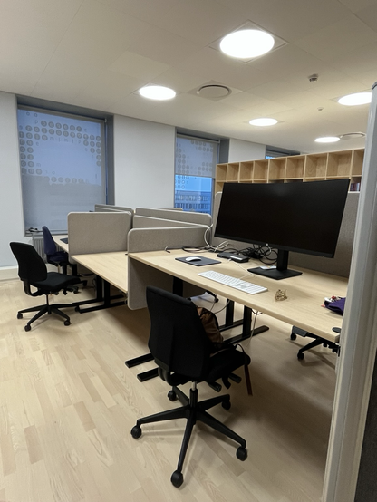 Kig ind til en bordrække i storrumskontoret. De enkelt borde er afskærmet af mindre, stofbetrukne skærme i lys, sandfarvet 