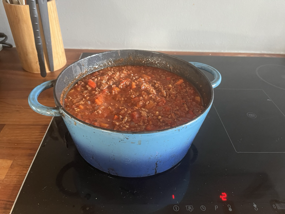 Blå smedejernsgryde fyldt med kødsovs med masser af tomat og grøntsager på et induktionskomfur