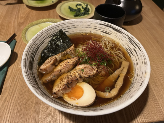 Nærbillede af en skål ramen med skiver af stegt kylling, et halvt æg, tang, nudler, purløg og bambus