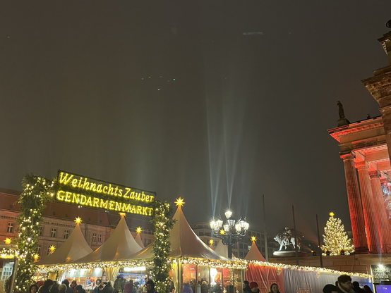 Indgang til Gendarmenmarkt markeret med neonlys med teksten “Weinachts Zauber”. Man kan se flere juletræer med lys, men ellers mest en tåget-grå himmel
