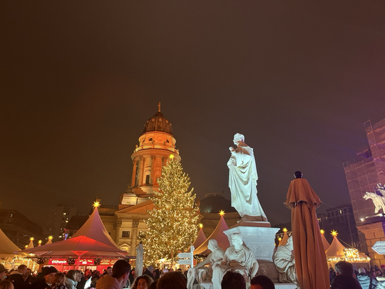 Et kirketårn (?) på Gendarmenmarkt med et flot oplyst, stort juletræ i forgrunde  og en hvid statue 