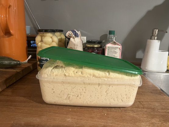 En bøtte med dej, just udtaget fra køleskabet, som er hævet nok til at låget er løftet af. I baggrunden remedier til julemad (glas med kogte kartofler, kirsebærsovs)