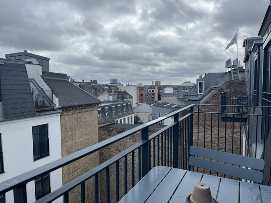 Udsigt fra balkonen over hustage i København. En overskyet himmel gør det hele lidt afdæmpet i farverne