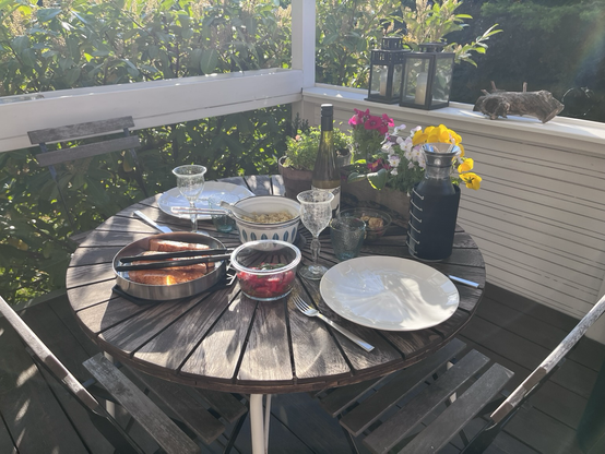 Terrassebord dækket til to personer med stegt laks, quinoa, tomatsalat og en rest grillede squash. Blomster og grønt i baggrunden 