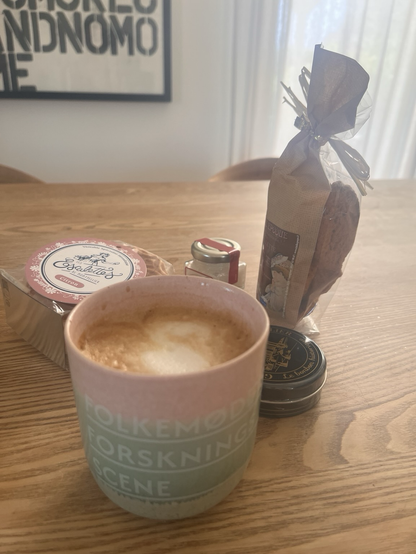 Smukt, håndlavet keramikkrus fra Folkemødets Forskningsscene med cappuccino i. Bagved franske citronsmåkager af form som vafler, et miniglas med Camargue-salt, en æske bolcher fra Montpellier og en pose med salte kiks af en slags