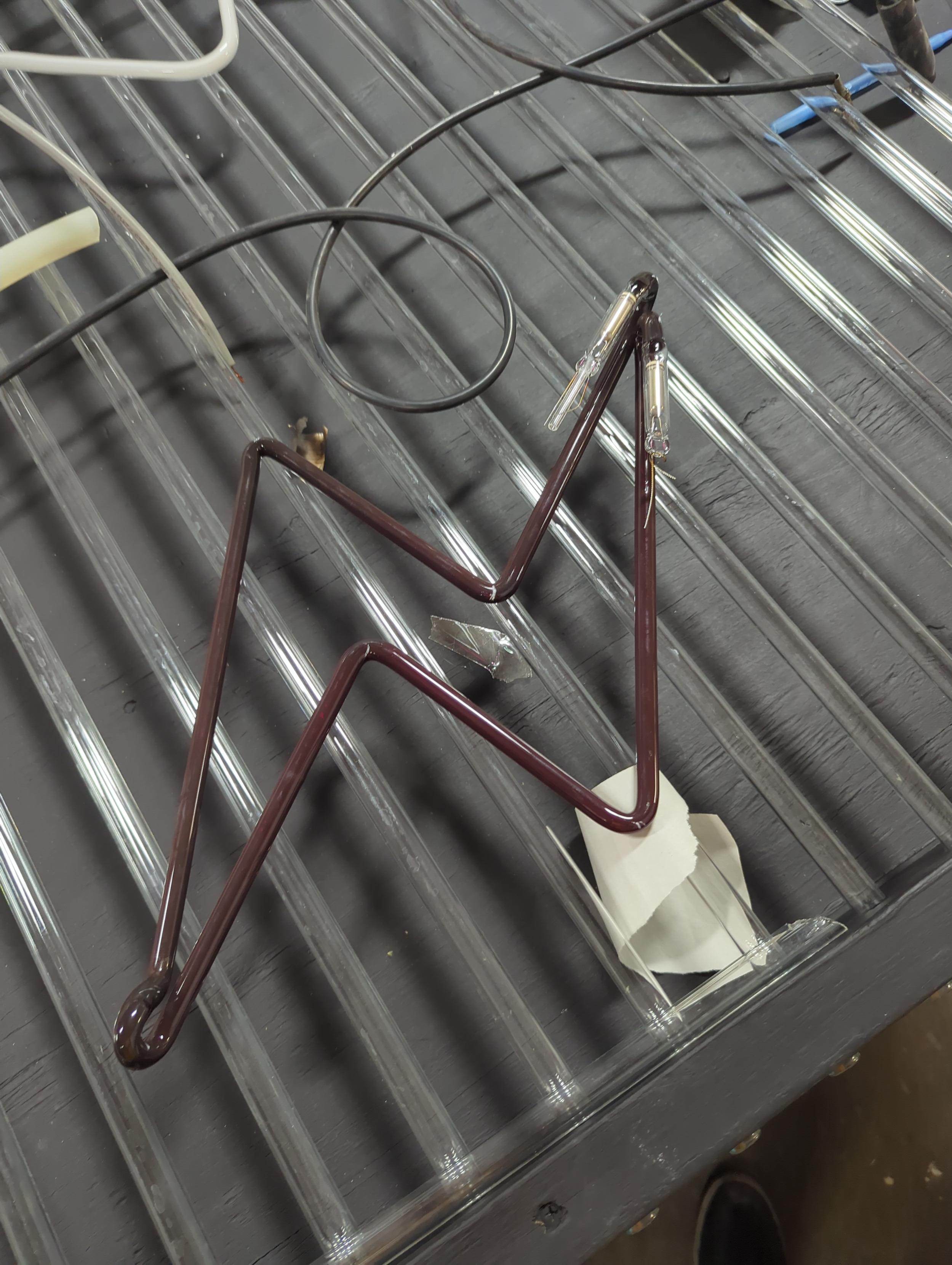 Dark red/ brown glass tube lightning bolt. The Oxblood Ruby. Black table in the background with glass tubes on it makes it easy to see any mercury spills