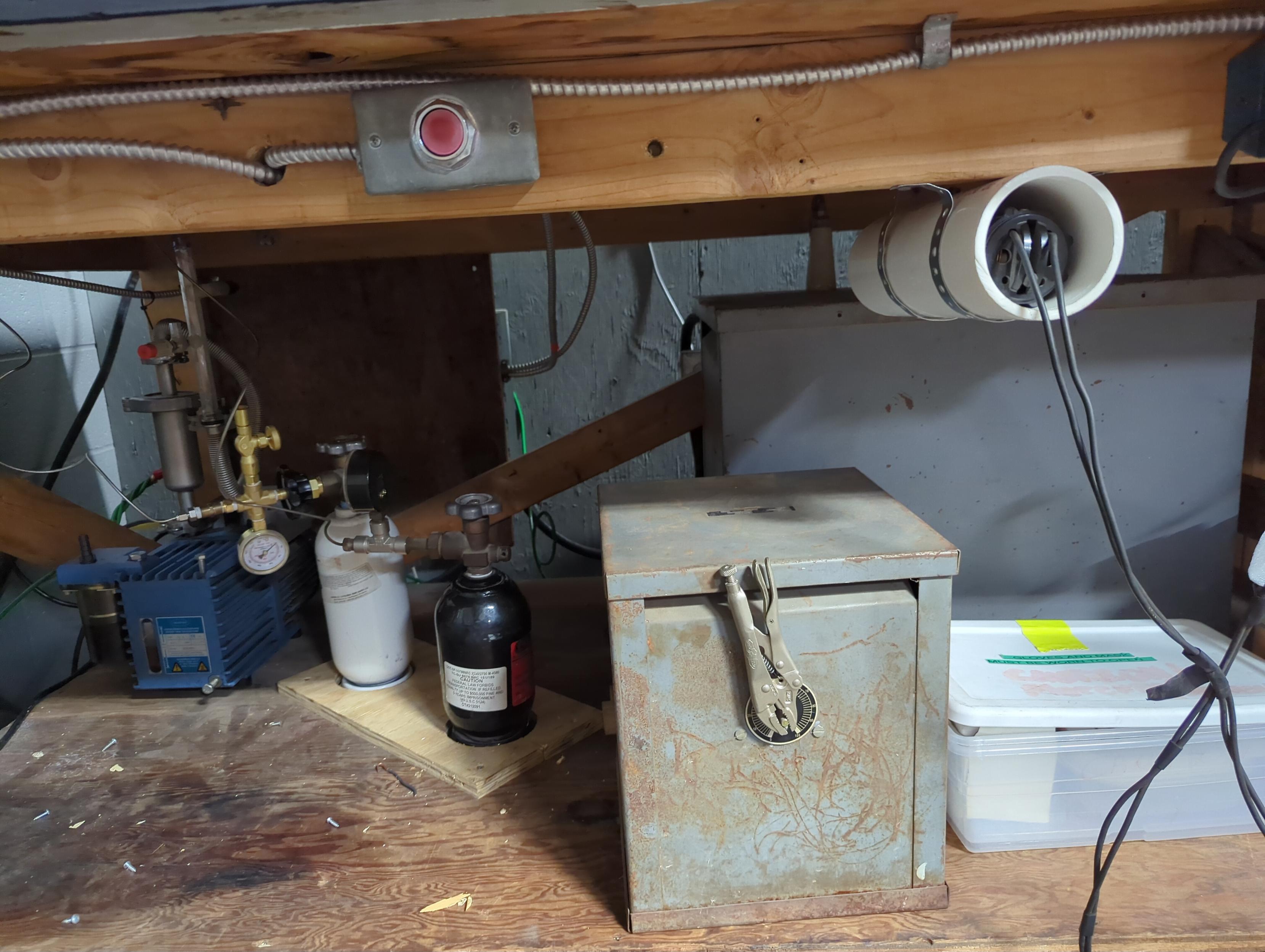 under the bombarder table, from left to right- blue box- dual stage Vacuubrand direct drive high vacuum pump. White bottle- high pressure UHP 99.999% Argon and the black bottle is Neon of the same pressure and purity. Above those is the second of two buttons- a system designed to keep the operators hands off of the manifold and from touching something they shouldnt. to rhe right of that is the hand held tesla "test" coil to find leaks. Underneath that is the choke, with a spinning vice grip handle. to the right of that is a series of airtight containers with about a pound of high purity mercury and a sketchy, but pure glass and stainless steel syringe. I really want them to get a new, more leak proof injector.