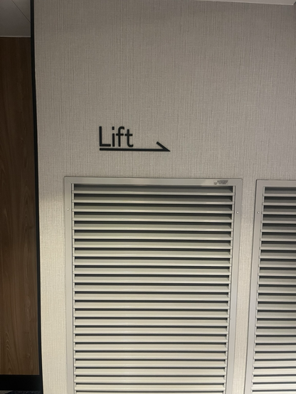 Skilt med pil til elevator på hvid væg med ordlyden: Lift